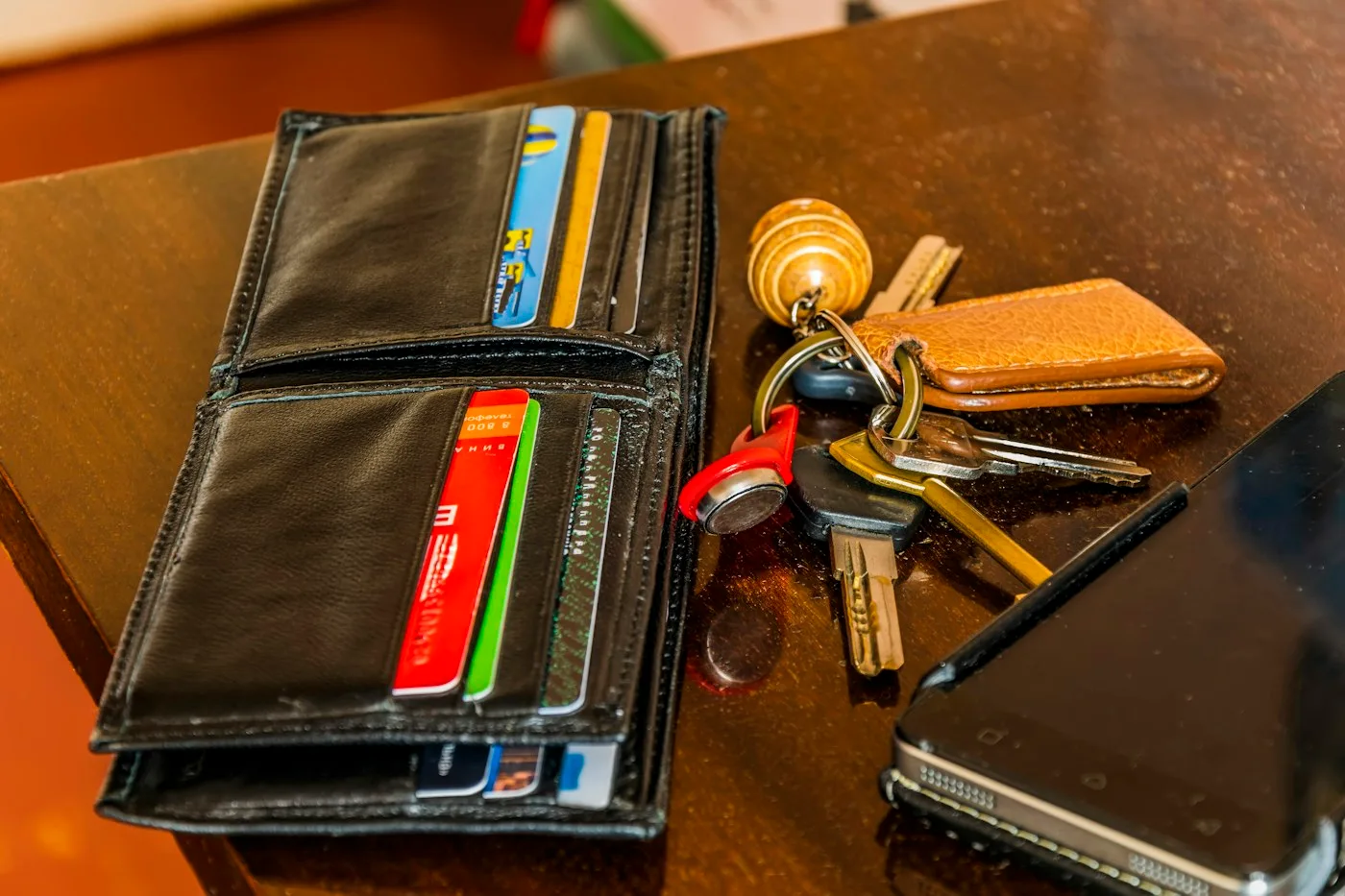 Keys, a wallet and a phone arranged on a wooden table