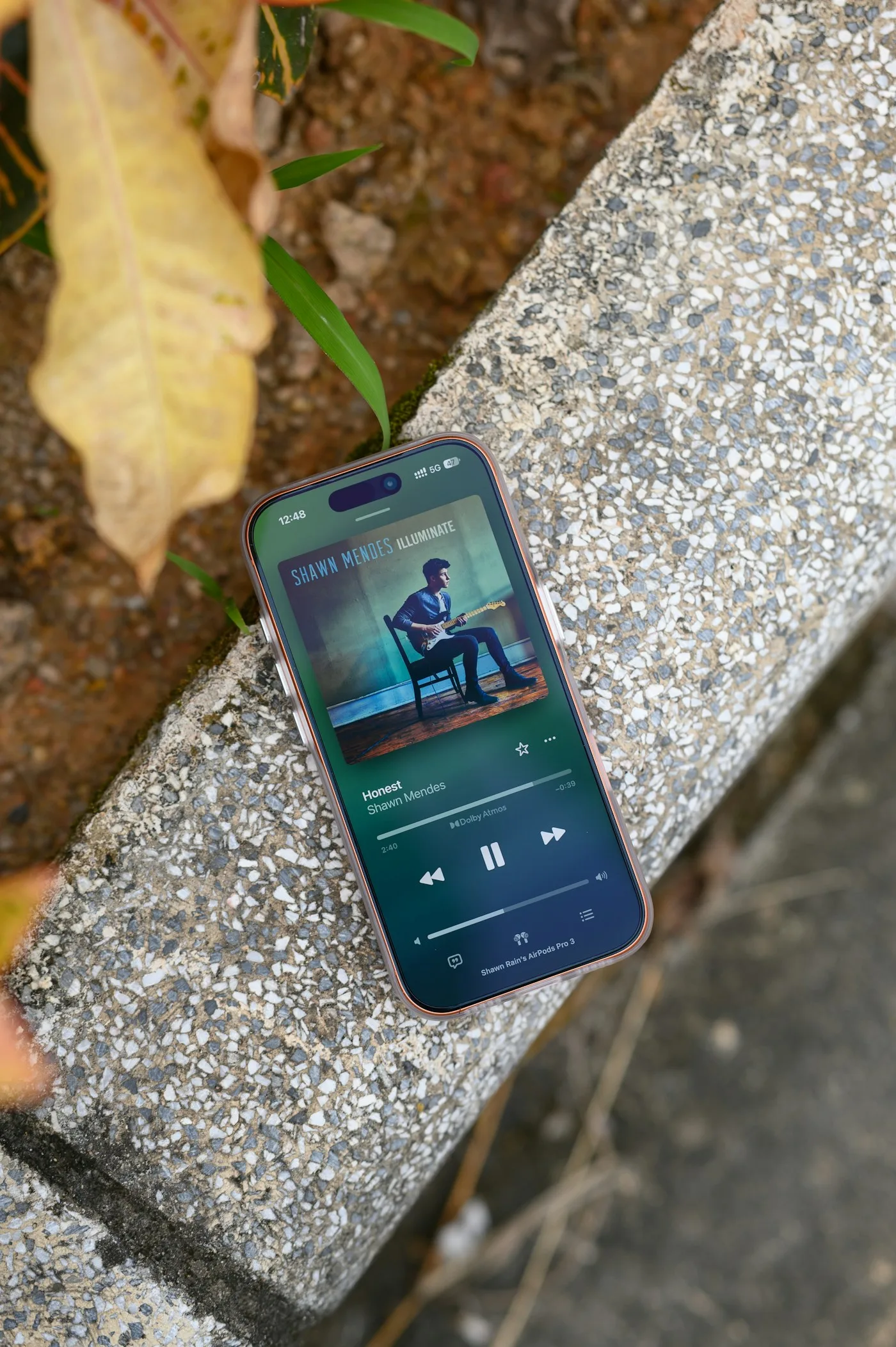 A smartphone showing a music player on a speckled stone ledge