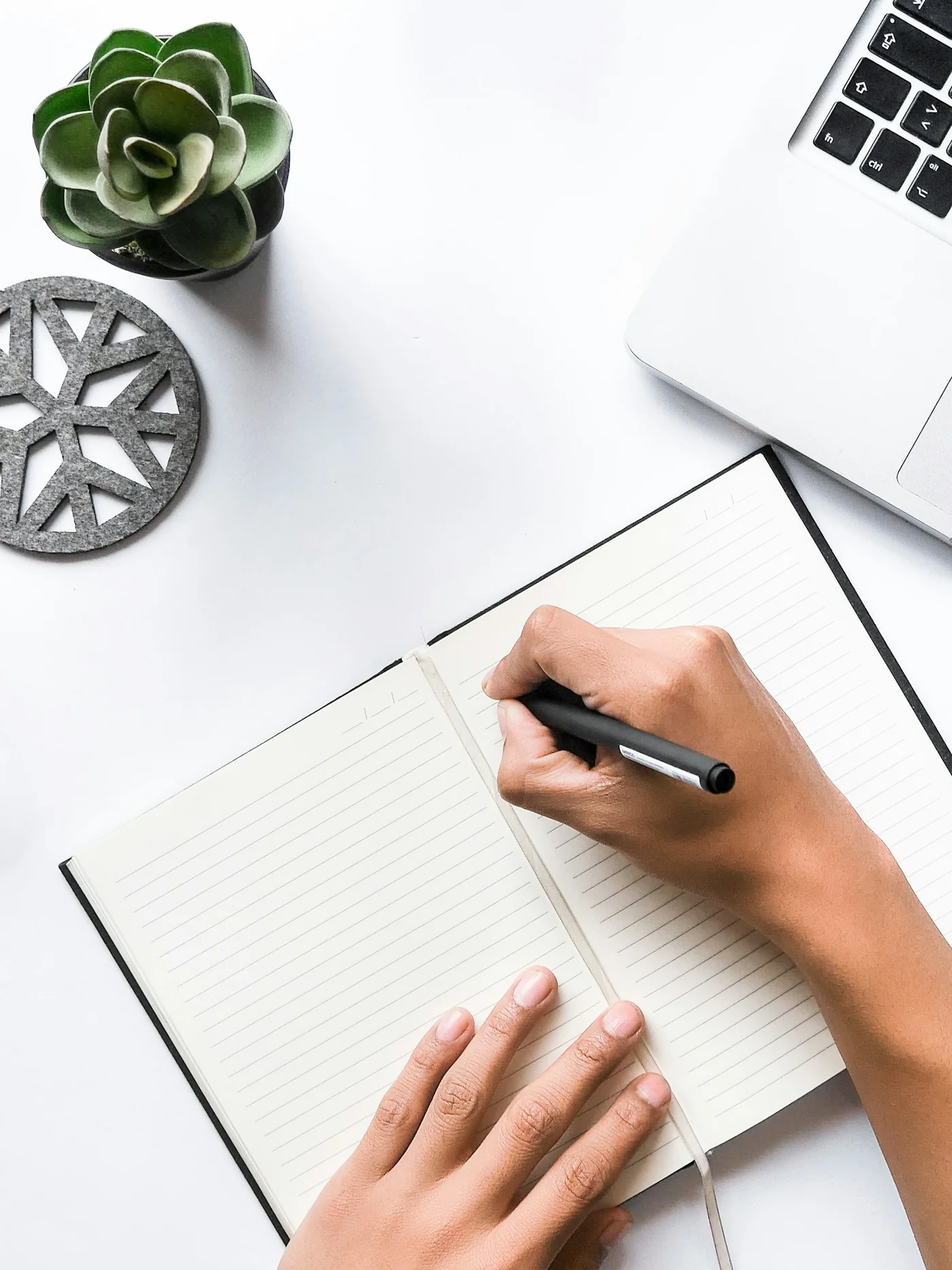 A person writing a short note in a white notebook